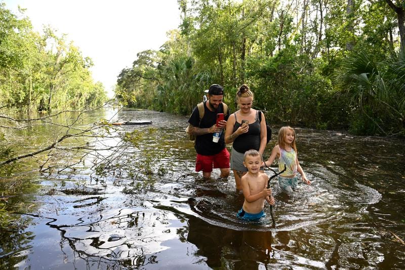 Dustin Holmes, rear left, his girlfriend Hailey Morgan, and her children Aria Skye Hall, 7, right, and Kyle Ross, 4, walk through a flooded road while returning to their home after Hurricane Helene passed near the area, Friday, Sept. 27, 2024, in Crystal River, Fla. (AP Photo/Phelan M. Ebenhack)