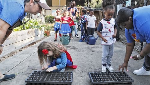 Germaine Appel (left), the school’s garden educator, and teacher Danielle Brown help kids plant seeds in the school garden on Sept. 11, 2019. Little Ones Learning Center in Forest Park is one of 18 state farm to school demonstration projects: Students grow and harvest food, and the school sells it to their parents and to the surrounding neighborhood. However, the little school can no longer sell its produce, after the city said it violated local codes. The property isn’t zoned for farm stands. BOB ANDRES / ROBERT.ANDRES@AJC.COM