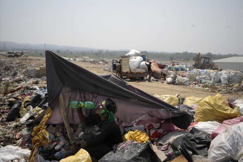 Mohmad Akram drinks water under shade during a heat wave at a garbage dump on the outskirts of Jammu, India, Wednesday, June 19, 2024. As many as 4 million people in India scratch out a living searching through landfills for anything they can sell. (AP Photo/Channi Anand)