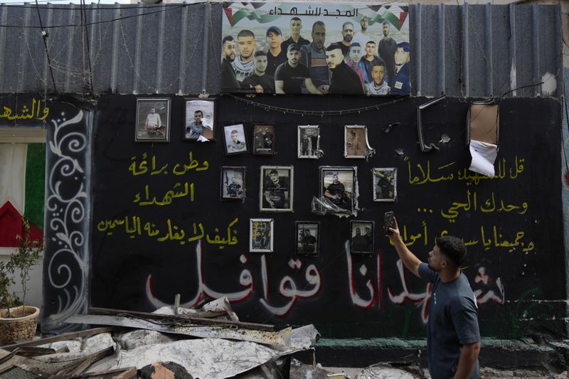 A man takes a picture of a wall displaying photos of Palestinians, who died during previous clashes, following an Israeli military operation in the West Bank refugee camp of Al-Faraa, Thursday, Aug. 29, 2024. (AP Photo/Nasser Nasser)