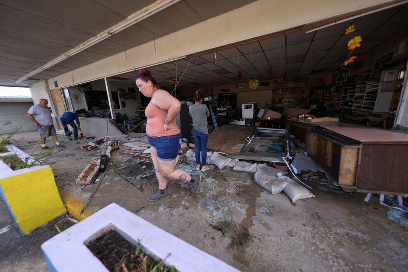 Kegan Ward, assistant manager of Swami Spirits, walks through debris of the damaged store in the aftermath of Hurricane Helene, in Cedar Key, Fla., Friday, Sept. 27, 2024. (AP Photo/Gerald Herbert)