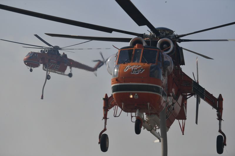 Two firefighting helicopters operate near Penteli, northeast of Athens, Greece, Monday, Aug. 12, 2024. Hundreds of firefighters backed by dozens of water-dropping planes and helicopters were battling the flames from first light Monday, with a major forest fire that began the previous day raging out of control on the fringes of Athens, fanned by strong winds. (AP Photo/Michael Varaklas)