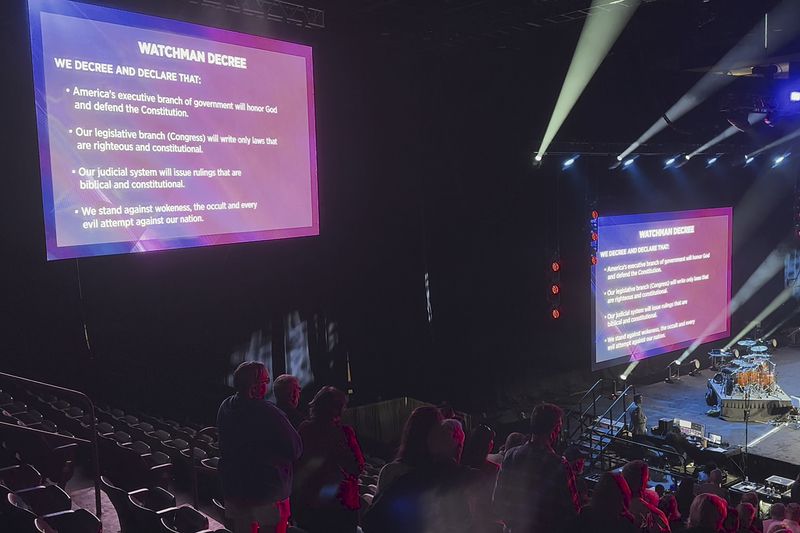 Attendees at the Opening the Heavens conference prepare to recite the "Watchman Decree," displayed on large screens and including a pledge to "take back and permanently control" positions of leadership in major areas of society, at the Mid-America Center in Council Bluffs, Iowa, on Friday, Sept. 13, 2024. (AP Photo/Peter Smith)