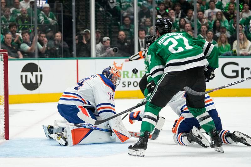 Edmonton Oilers goaltender Stuart Skinner (74) defends against an airborne puck under pressure from Dallas Stars left wing Mason Marchment (27) during the first period of Game 1 of the Western Conference finals in the NHL hockey Stanley Cup playoffs Thursday, May 23, 2024, in Dallas. (AP Photo/Tony Gutierrez)