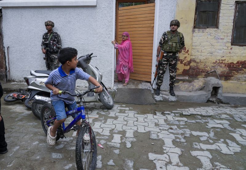 Indian paramilitary soldiers guard as a boy rides on his bicycle during the door-to-door election campaigning by Bharatiya Janata Party (BJP) candidate ahead of the Jammu and Kashmir state assembly elections in Srinagar, Indian controlled Kashmir,Thursday, Aug. 29, 2024. (AP Photo/Mukhtar Khan)