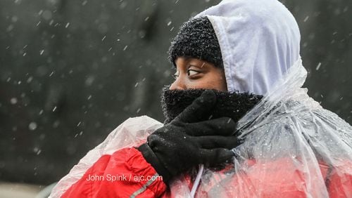 Trina Cloud, who works security, protects her face from the snow and sleet mix falling at Mercedes- Benz Stadium, where Georgia high school football is underway.