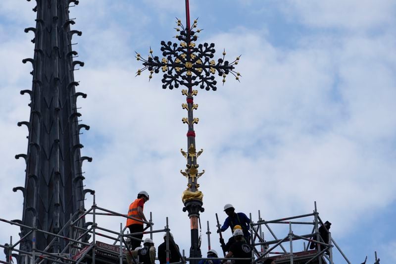 Workers install Notre Dame de Paris cathedral's Croix du Chevet in front of the cathedral spire, left, Friday, May 24, 2024, in Paris. The Croix du Chevet is the only piece of the cathedral roof that did not burn in the devastating April 2019 fire. (AP Photo/Thibault Camus)