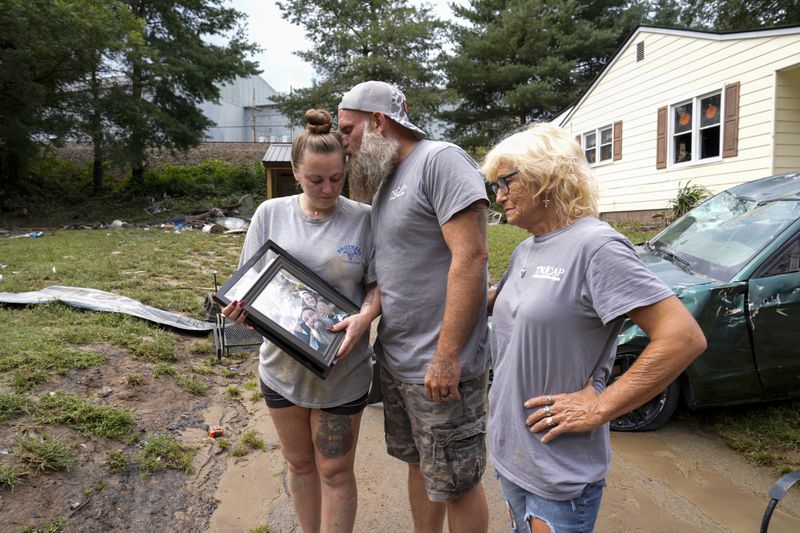 Dustin Bentley, center kisses his wife Jennifer Bentley, left, after retrieving family photos from their flood damaged home as his mother Janet Sams looks on Saturday, Sept. 28, 2024, in Newport, Tenn. (AP Photo/George Walker IV)