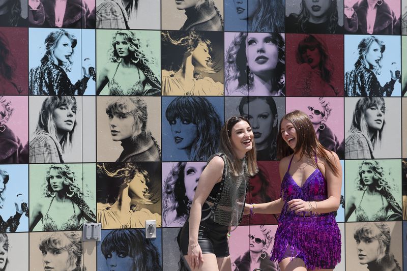 Wearing Taylor Swift attire, Megan Webb, left, of Smyrna, and Morgan Lewis, of Woodstock, react as they pose for a picture in front of the Taylor Swift merchandise bus at Mercedes-Benz Stadium, Friday, April 28, 2023, in Atlanta. Taylor Swift and Janet Jackson will perform next door to one another Friday night, Jackson at State Farm Arena and Swift at Mercedes-Benz Stadium. (Jason Getz / Jason.Getz@ajc.com)