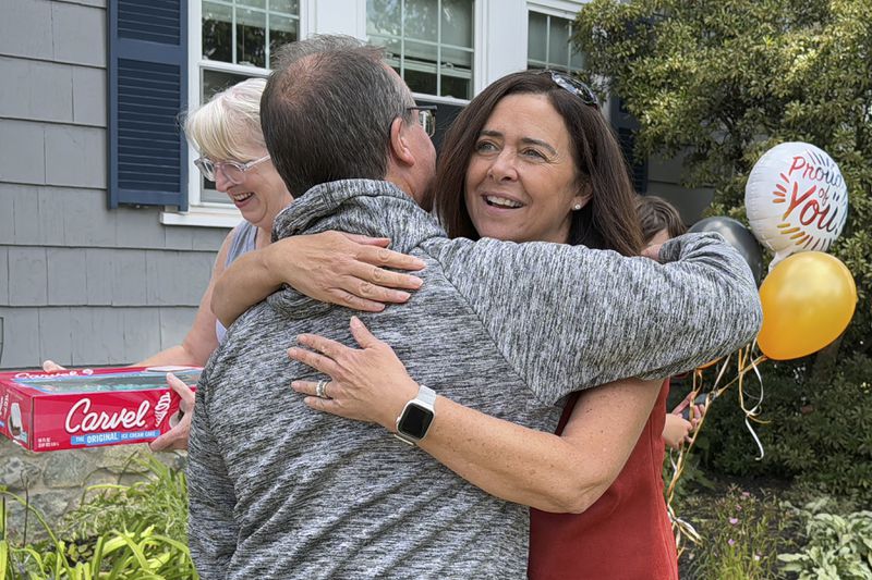 Lori Talanian, right, director of corporate partnerships at Ira Cars, hugs John Quill, center, director and coach of the Boston Bear Cubs hockey team, Wednesday, Aug. 21, 2024, after her company presented the team with a donation of $3,900, at the Doherty family home, in Norwood, Mass. (AP Photo/Michael Casey)