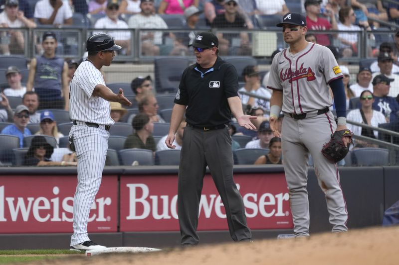 New York Yankees third base coach Luis Rojas, left, argues with the umpire, center, about a tagging call against Anthony Volpe during the sixth inning of a baseball game against the Atlanta Braves, Sunday, June 23, 2024, in New York. (AP Photo/Pamela Smith)
