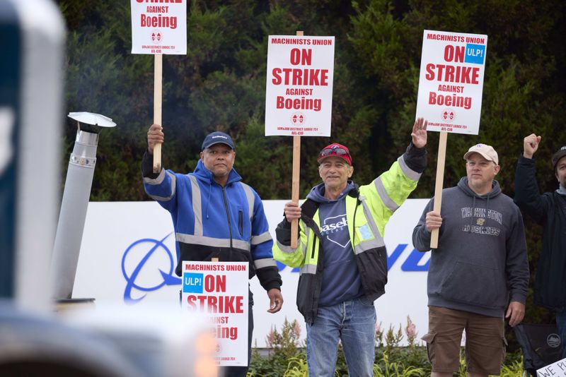 Boeing Machinists Union members Steven Wilson, left, Dave Hendrickson, center,, and Mark Erickson, right, wave to passing traffic while on the picket line at the Renton assembly plant, Friday, Sept. 13, 2024, in Renton, Wash. (AP Photo/John Froschauer)