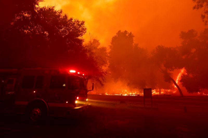 A fire engine is driven past a fire-engulfed structure as crews battle the Airport Fire Tuesday, Sept. 10, 2024, in El Cariso, an unincorporated community in Riverside County, Calif. (AP Photo/Etienne Laurent)