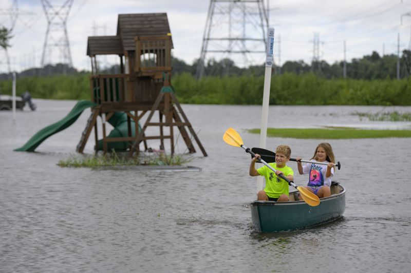 Siblings Avery, 10, and Grace LeBlanc, 7, canoe in their backyard next to playground equipment after flooding from Hurricane Francine in Montz, La., in St. Charles Parish, Thursday, Sept. 12, 2024. (AP Photo/Matthew Hinton)