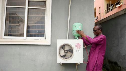 A technician positions an R-22 refrigerant on an outdoor air conditioning unit in Lagos, Nigeria, Thursday, July 18, 2024. (AP Photo/Sunday Alamba)
