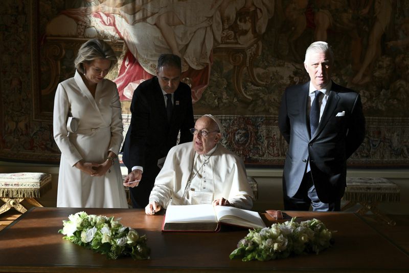 Pope Francis, center, signs the book of honor during his visit to King Philippe of Belgium, right, and Queen Mathilde at the Castle of Laeken, Belgium, Friday, Sept. 26, 2024, on the second day of a four-day apostolic journey to Luxembourg and Belgium. (Alberto Pizzoli/pool photo via AP)