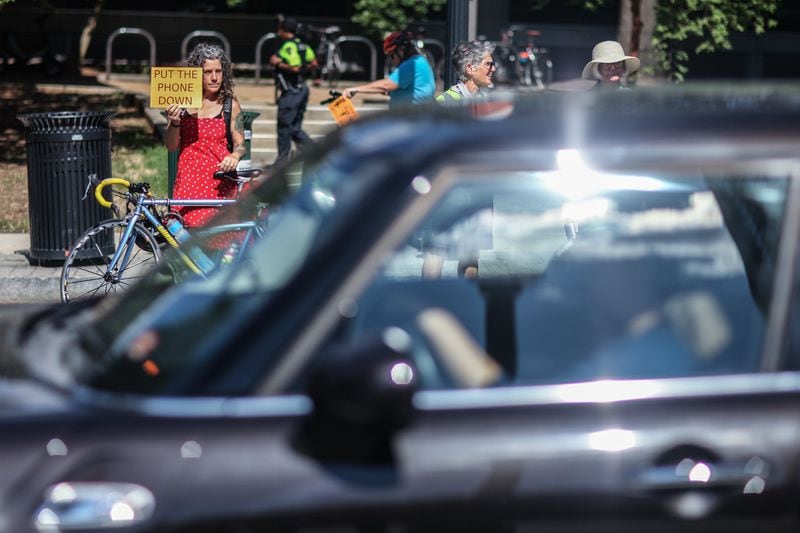 Kat Jones, left, holds a sign during a rally on West Peachtree Street near 15th Street on Wednesday, July 24, 2019, in Atlanta. The location is where William Alexander was hit and killed by a bus while riding on a scooter on July 17. Organizers joined together as a “human protected sidewalk, bike and scooter lane” demanding the city prioritize protected bike and scooter lanes. BRANDEN CAMP/SPECIAL