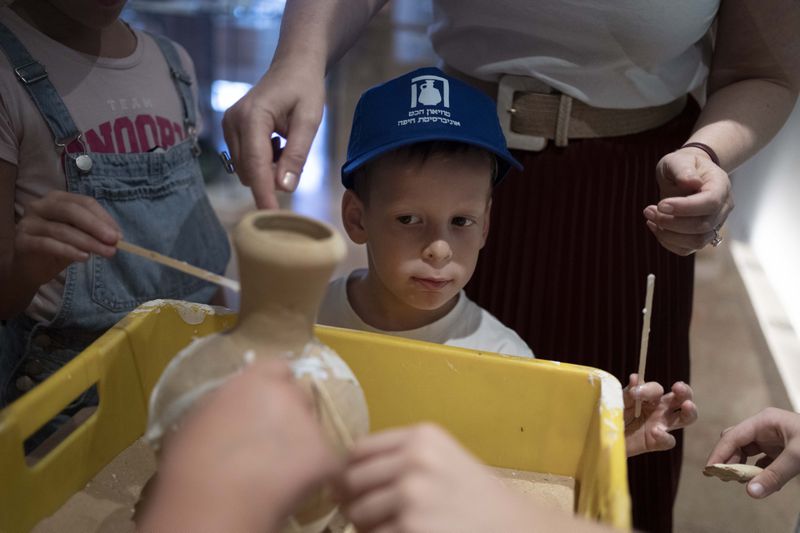 Ariel Heller, 4, helps to glue a broken clay jar during a special tour with his family after he accidentally broke another jar at the Reuben and Edith Hecht Museum in Haifa, Israel, Friday, Aug. 30, 2024. The boy who accidentally broke a rare 3,500-year-old jar in an Israeli museum has been forgiven and invited back, as curators hope to turn the disaster into a teachable moment. (AP Photo/Maya Alleruzzo)