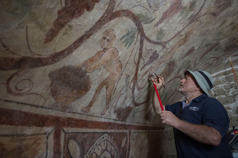 A worker touches up an ancient wall drawing of Greek goddess Demeter at an archeological tomb site in Ashkelon, Israel, Tuesday Aug. 27, 2024. The tomb where the painting was found is at least 1,700 years old, says the Israeli Antiquities Authority, whose workers are restoring the site. (AP Photo/Ohad Zwigenberg)