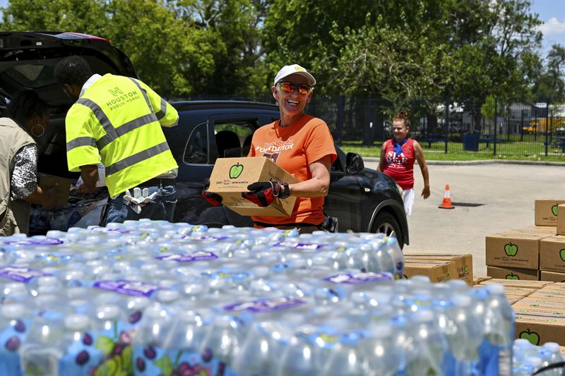 Volunteer Karen Jones, center, helps to hand out supplies at Acres Homes cooling center in Houston, Wednesday, July 10, 2024. After Hurricane Beryl slammed into Texas, knocking out power to nearly 3 million homes and businesses. (AP Photo/Maria Lysaker)