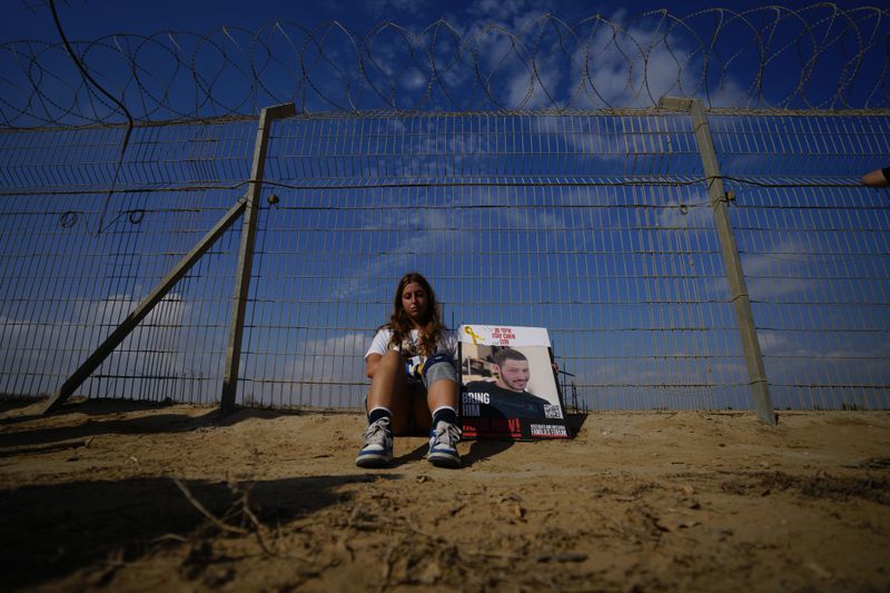 A woman sits next to a fence as relatives and friends of hostages held in the Gaza Strip by the Hamas militant group take part in a protest calling for their release in the kibbutz Nirim, southern Israel, Thursday, Aug. 29, 2024. (AP Photo/Tsafrir Abayov)