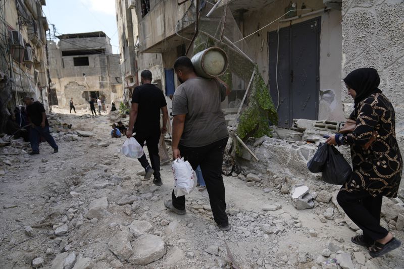 Palestinian refugees walk through the rubble of destroyed houses while they flee their homes during the Israeli army operation in the West Bank refugee camp of Tulkarem, in Tulkarem, Thursday, Sept. 5, 2024. (AP Photo/Nasser Nasser)