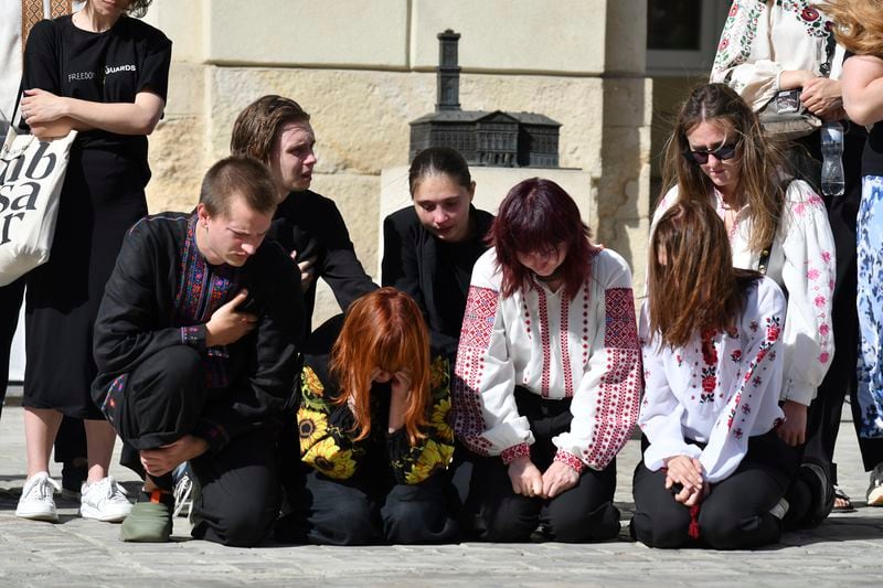 People kneel in respect during the funeral ceremony of Yaroslav Bazylevych's family members in Lviv, Ukraine, Friday, Sept. 6, 2024. Bazylevych's wife Yevgenia and their three daughters - Darina, 18, Emilia, 7, and Yaryna, 21 - were killed in Wednesday's Russian missile attack. (AP Photo/Mykola Tys)