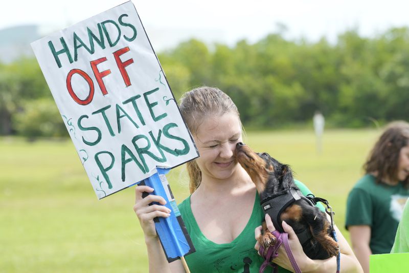 Bonnie, a seven-month-old dachshund, licks Alexandra Maxwell's face as they a protest against Gov. Ron DeSantis' plan to develop state parks with business ventures such as golf courses, pickleball courts and large hotels, during a demonstration at Oleta River State Park, Tuesday, Aug. 27, 2024, in North Miami Beach, Fla. (AP Photo/Wilfredo Lee)