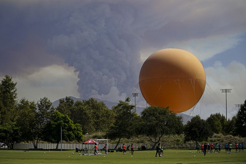 A plum of smoke created by the Airport Fire rises over a group playing soccer Tuesday, Sept. 10, 2024, in a view from Irvine, Calif. (AP Photo/Eugene Garcia)