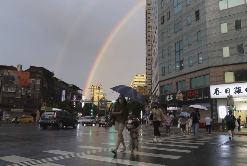 People walk in the rain with a backdrop of the rainbow in the sky as Typhoon Krathon approaches to Taiwan in Taipei, Monday, Sept. 30, 2024. (AP Photo/Chiang Ying-ying)