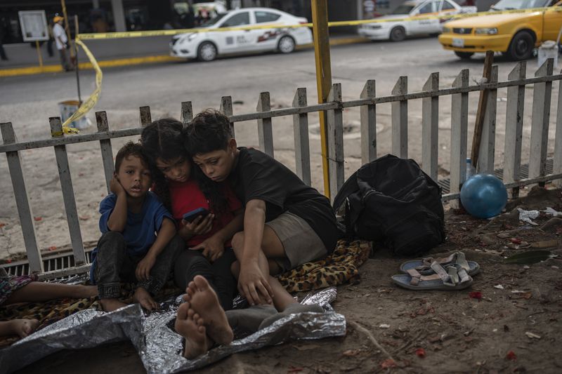 The Bolaños children, from Venezuela, watch videos on a mobile phone outside the bus terminal where they are living with their single mother Keilly and one other sibling, along with other migrants in Villahermosa, Mexico, Saturday, June 8, 2024. Their mother was captured in the northern state of Juarez, where she said she was beaten by the military in front of her children, loaded on a bus for two days, and left in Villahermosa. (AP Photo/Felix Marquez)