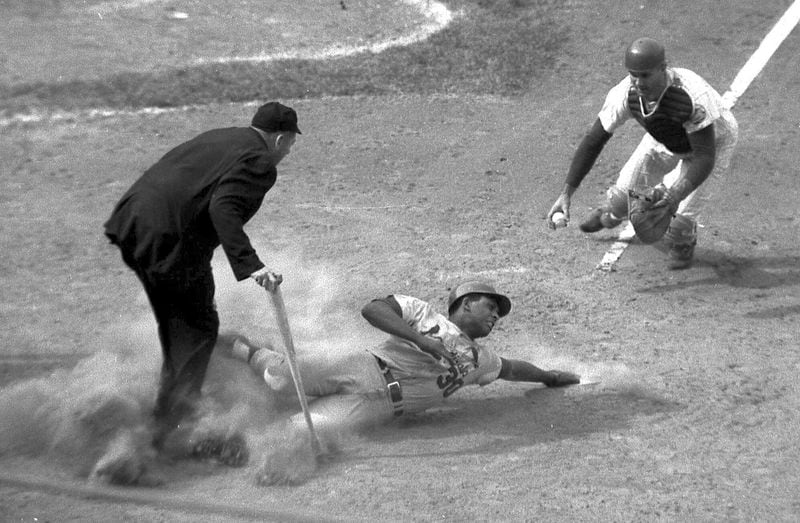 St. Louis Cardinals' Orlando Cepeda scores in the eighth inning of a baseball game as New York Mets catcher J.C. Martin, right, and umpire Tim McCarver, left, watch at Shea Stadium in New York in 1968. Cepeda, the slugging first baseman nicknamed “Baby Bull” who became a Hall of Famer among the early Puerto Ricans to star in the major leagues, has died. He was 86. The San Francisco Giants and his family announced the death Friday night, June 28, 2024, and a moment of silence was held on the scoreboard at Oracle Park midway through a game against the Los Angeles Dodgers. (AP Photo, File)