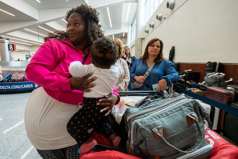 Joann Pierre, (left), of New Jersey, waits in line with her 1-year-old daughter, Isabella Maloi, to get their luggage back in the south terminal in Hartsfield-Jackson Atlanta International Airport in Atlanta on July 21.  (Ziyu Julian Zhu/The Atlanta Journal-Constitution)