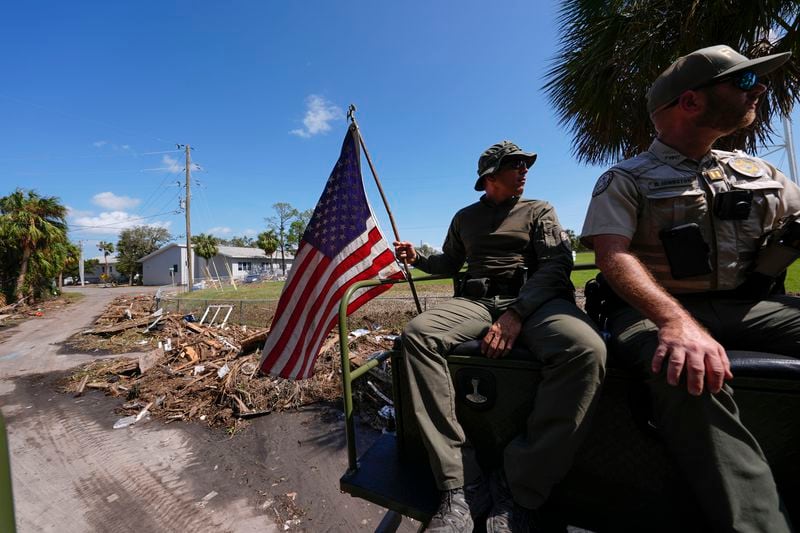 Officer Nate Martir, a law enforcement officer from the Florida Fish Wildlife and Conservation Commission, holds an American flag that was lying on the ground amid debris, while patrolling from a high water capable swamp buggy, in the aftermath of Hurricane Helene, in Cedar Key, Fla., Friday, Sept. 27, 2024. (AP Photo/Gerald Herbert)