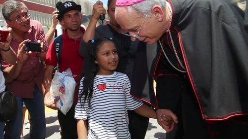 FILE - El Paso Catholic Bishop Mark Seitz talks with Celsia Palma, 9, of Honduras, as they walked to the Paso Del Norte International Port of Entry, Thursday, June, 27, 2019, in Juarez, Mexico. (AP Photo/Rudy Gutierrez)