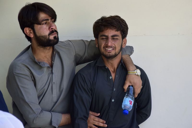 A man comforts another, who mourns over the death of his family member, killed by gunmen at a highway in Musakhail, at a hospital, in Quetta, Pakistan, Monday, Aug. 26, 2024. (AP Photo/Arshad Butt)