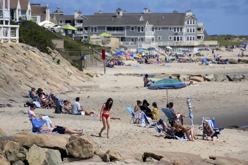 People sit on the beach, Friday, Aug. 30, 2024, in Dennis Port, Mass. (AP Photo/Michael Dwyer)