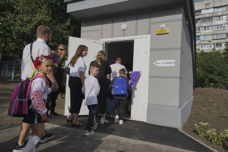 Schoolchildren and their parents enter an underground school on the first day at school in Kharkiv, Ukraine, Monday, Sept. 2, 2024. The purpose-built "bunker school" aims to provide a learning environment safe from Russian everyday airstrikes. (AP Photo/Andrii Marienko)