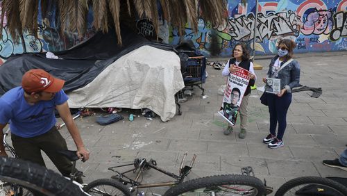 Catholic nun Paola Clericó, holding a poster of missing person Fernando Ivan Ornelas, and Veronica Rosas with a photo of her missing son Diego, ask a resident if he recognizes either man and invite him to join a Mass with members of their search collective "Uniendo Esperanzas" or Uniting Hope, in Mexico City, Sunday, July 21, 2024. The collective of people with missing family members held a Mass on the birthday of Ornelas who disappeared five years prior. (AP Photo/Ginnette Riquelme)