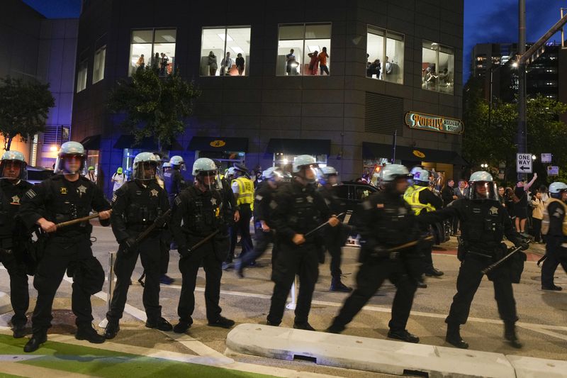 People watch from the second floor of a building as police block the street during a demonstration near the Israeli Consulate during the Democratic National Convention Tuesday, Aug. 20, 2024, in Chicago. (AP Photo/Julio Cortez)