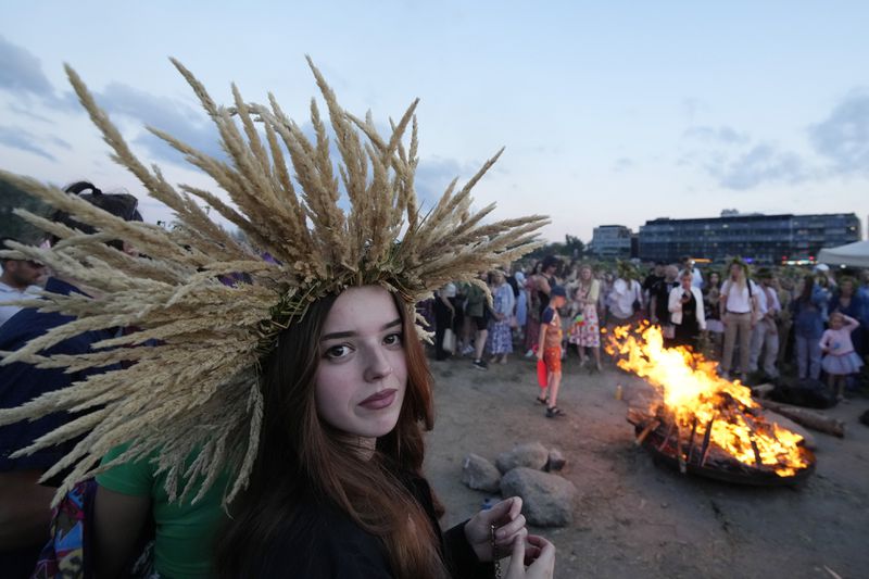 A young Ukrainian woman wears an ear of grain braid during a traditional Ukrainian celebration of Kupala Night, in Warsaw, Poland, on Saturday, June 22, 2024. Ukrainians in Warsaw jumped over a bonfire and floated braids to honor the vital powers of water and fire on the Vistula River bank Saturday night, as they celebrated their solstice tradition of Ivan Kupalo Night away from war-torn home. (AP Photo/Czarek Sokolowski)