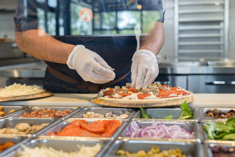 Wearing food-safe gloves, an employee at Blaze Pizza assembles ingredients for a custom pie. (Courtesy of Blaze Pizza)