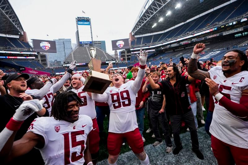 Washington State defensive tackle Bryson Lamb (99) holds up the Apple Cup Trophy while celebrating with running back Djouvensky Schlenbaker (15) and edge Nusi Malani, far right, after beating Washington 24-19 in an NCAA college football game Saturday, Sept. 14, 2024, in Seattle. (AP Photo/Lindsey Wasson)