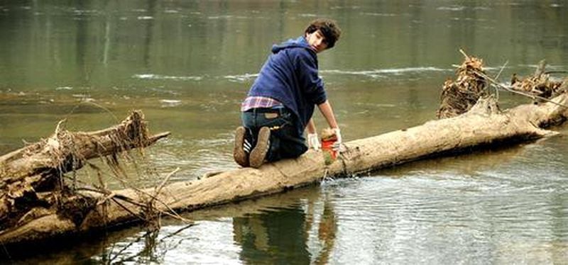 Julian Gindi, perched on a fallen tree, empties out a plastic bottle before bagging it up with other trash he and his buddies collected along the banks of the Chattahoochee River.