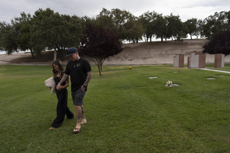 Mikayla Brown, left, and her husband, Tyler, hold hands as they walk toward their car after visiting the grave of their son, Elijah, who died of a fentanyl overdose at 15, in Paso Robles, Calif., Friday, Aug. 2, 2024. (AP Photo/Jae C. Hong)