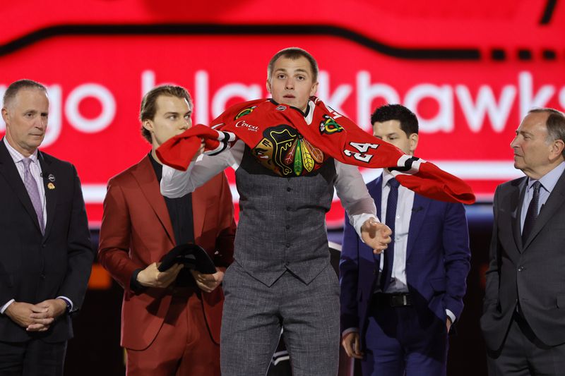 Artyom Levshunov, center, puts on a jersey after being selected by the Chicago Blackhawks during the first round of the NHL hockey draft Friday, June 28, 2024, in Las Vegas. (AP Photo/Steve Marcus)