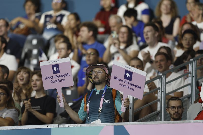 A volunteer for the Paralympic Games holds two signs reading "Silence s'il-vous-plaît, Quiet Please" during the mens' United States versus France goalball game during the Paralympic Games in Paris on Saturday, Aug. 31, 2024. Football fans are known for being loud and rowdy. But the Paralympic sports most closely related to football, blind football and goalball, require spectators to be silent during game action so that players can receive audible cues from the ball and the environment. (AP Photo/Felix Scheyer)