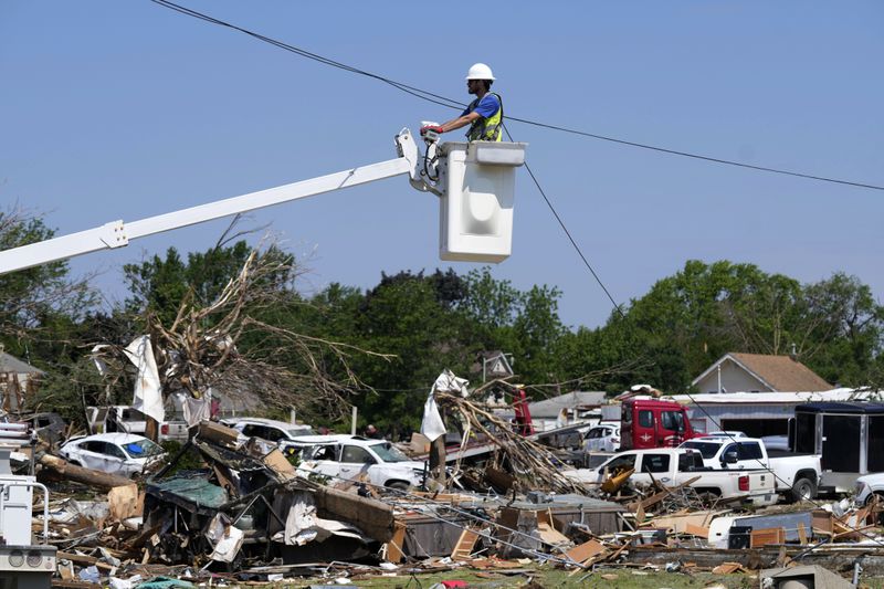 A worker fixes a line above debris from tornado damaged homes, Wednesday, May 22, 2024, in Greenfield, Iowa. (AP Photo/Charlie Neibergall)