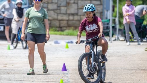 Instructor Ashley Clarkin watches Mang Bor Cin weave her bike through the cones during Mang Bor Cin's first bike riding lesson in Decatur Saturday. July 23, 2023.  (Steve Schaefer/steve.schaefer@ajc.com)