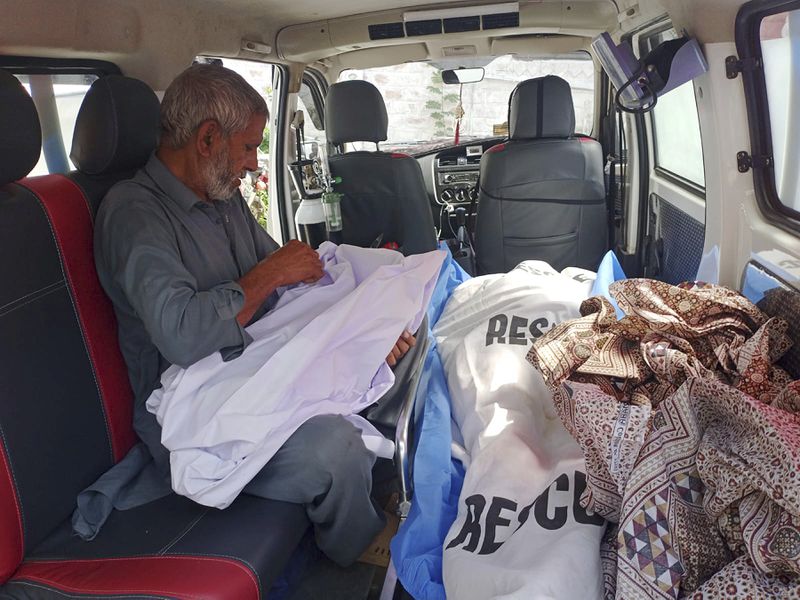 A relative inside an ambulance, carries body of a child next to the body of his mother, who were killed as a passenger bus fell into a ravine, on the arrival at a hospital in Kahuta, Pakistan, Sunday, Aug. 25, 2024. (AP Photo/Mohammad Yousaf)